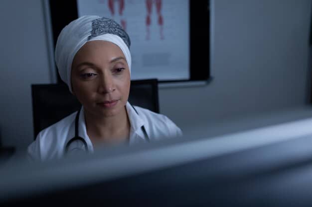 A close-up photograph of a tired nurse looking at a computer screen in a dimly lit hospital room, highlighting the emotional and physical strain of the nursing shortage.